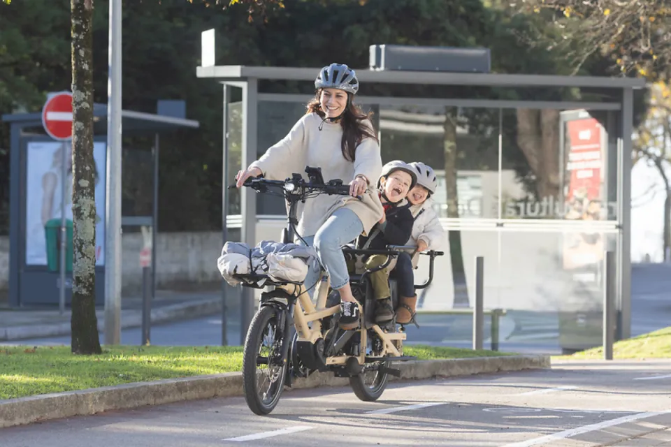 Woman riding Tern GSD Gen 3 family e-cargo bike while carrying two kids on the rear rack